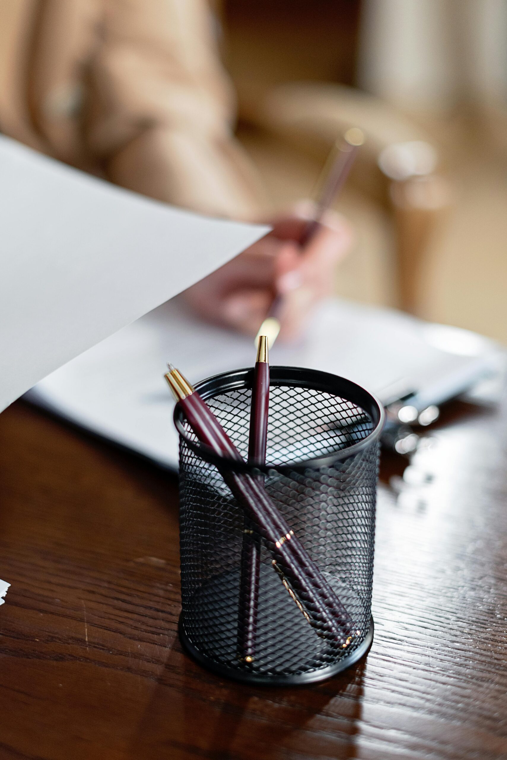 Close-up of an office desk with pens, paper, and a person writing, ideal for business themes.